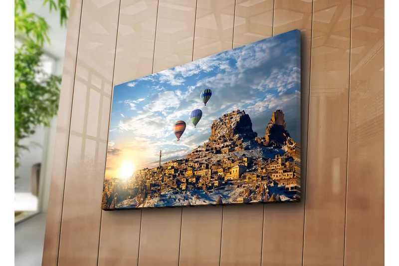 Canvas-taulu 70x45 cm - Värikkäät kuumailmapallot leijuvat viehättävän vuoristokylän yllä auringonnousun aikaan, Kulta / Sininen / Oranssi