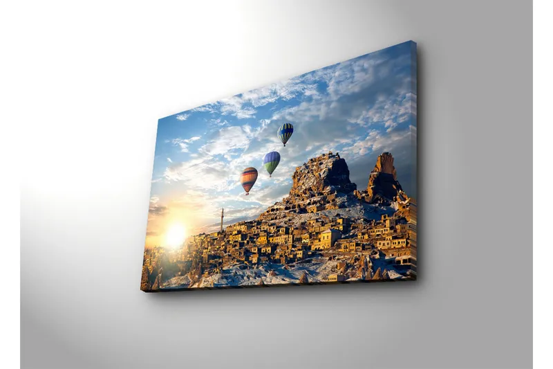 Canvas-taulu 70x45 cm - Värikkäät kuumailmapallot leijuvat viehättävän vuoristokylän yllä auringonnousun aikaan - Kulta / Sininen / Oranssi - Sisustustuotteet - Taulu & taide - Canvas-taulu