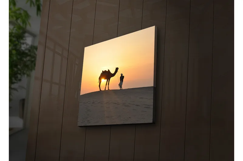 Canvas-taulu LED-valaistuksella 28x28 cm - Kameli ja mies auringonlaskussa hiekkadyyneillä, Oranssi / Keltainen / Musta