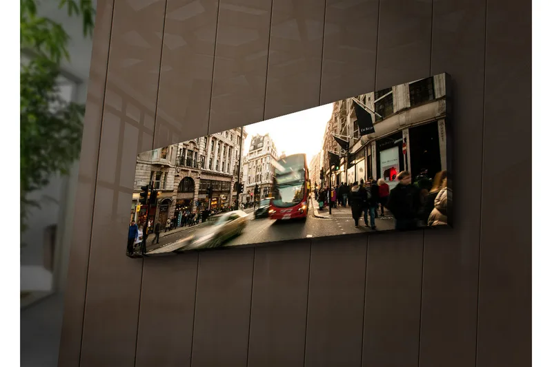 Canvas-taulu LED-valaistuksella 30x90 cm - Vilkas kaupunkikuva, jossa on liikettä ja ihmisiä kadulla, Punainen / Beige / Vihreä