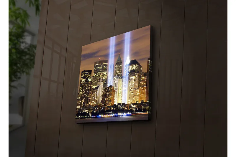 Canvas-taulu LED-valaistuksella 40x40 cm - Kaupunkikuva valonsäteineen, jotka symboloivat kadonneiden elämien muistoa, Kulta / Sininen / Musta