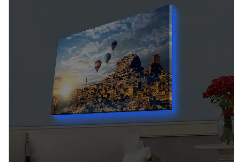 Canvas-taulu LED-valaistuksella - Värikkäät kuumailmapallot leijuvat vuoristoisen maiseman yllä auringonlaskun aikaan, Kulta / Sininen / Oranssi