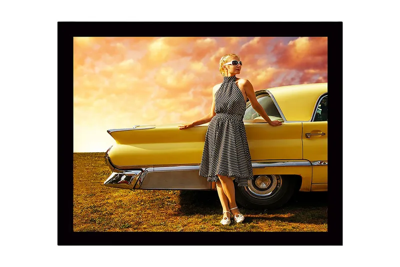 Kehystetty puinen canvas-taulu - 41x56 cm - Nainen pilkullisessa mekossa nojaa vanhaan autoon, Keltainen / Musta / Valkoinen